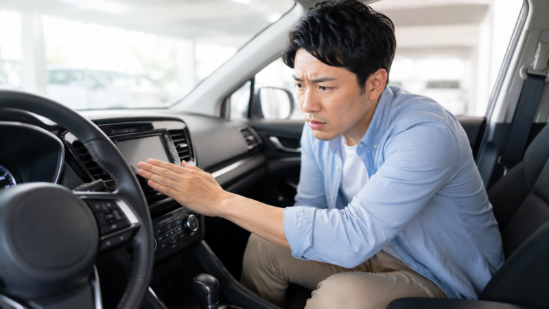 車のエアコン吹き出し口で冷えを確認する男性
